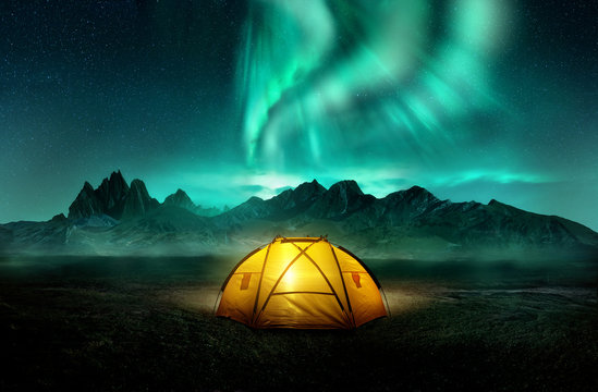 A glowing yellow camping tent under a beautiful green northern lights aurora. Travel adventure landscape background. Photo composite.