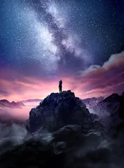 Langzeitbelichtungslandschaft des nächtlichen Himmels. Ein Mann, der auf einem hohen Felsen steht und die Sterne beobachtet, die in den Nachthimmel aufsteigen. Foto zusammengesetzt. © James Thew
