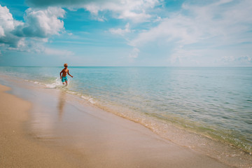 happy young boy run and play with waves on beach