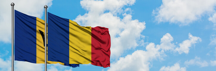 Barbados and Romania flag waving in the wind against white cloudy blue sky together. Diplomacy concept, international relations.