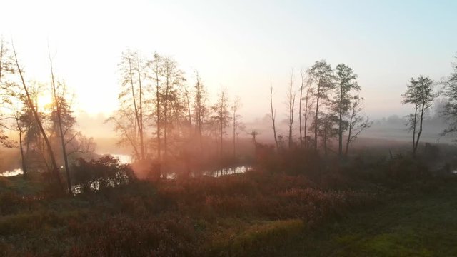 Misty scene of  riverbed and meadows near river.Nida River valley in Poland early morning view. Flight to sun above trees.  Aerial drone footage. Yellow orange sunrise horizon. Romantic relaxing mood.