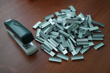 Many clips for a stapler on a wooden table. Stapler with a bunch of paper clips on the table.