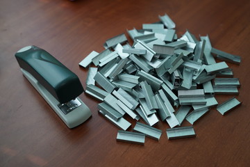 Many clips for a stapler on a wooden table. Stapler with a bunch of paper clips on the table.