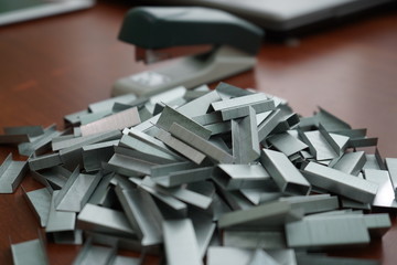 Many clips for a stapler on a wooden table. Stapler with a bunch of paper clips on the table.
