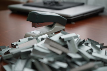 Many clips for a stapler on a wooden table. Stapler with a bunch of paper clips on the table.