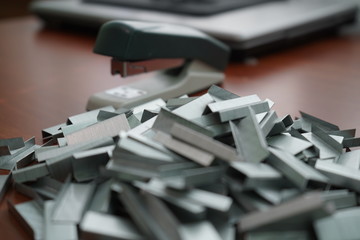 Many clips for a stapler on a wooden table. Stapler with a bunch of paper clips on the table.