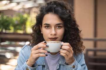 Hot coffee. Beautiful young girl drinking tea or coffee in cafe. Beauty model woman with the cup of hot beverage. There is place for your logo on the cup.