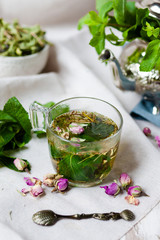 Traditional hot mint moroccan tea served in a transparent cup. Metal teapot with fresh mint on the background. Dry leaves and vintage spoon as decor. Gentle herbal detox, natural depressant