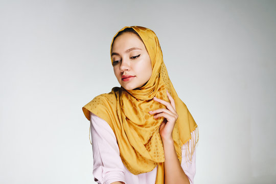 a Muslim woman in a yellow scarf modestly lowered her eyes. studio light gray