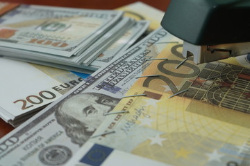 The stapler fastens the dollar and euro notes with iron clips. Stapler with paper clips on the background of banknotes.
