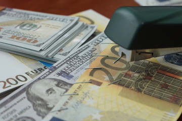The stapler fastens the dollar and euro notes with iron clips. Stapler with paper clips on the background of banknotes.