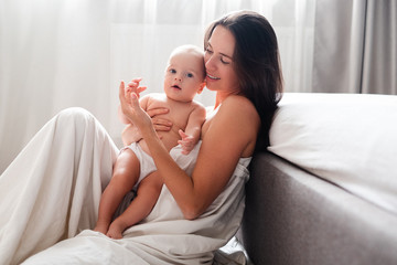 Mother and her baby son lying in bed on white sheets. Top view.