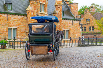Rear view, back view of horse-drawn carriage goes to the direction of old brick buildings, Bruges, Belgium.