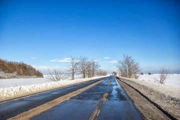 Landscape with a road in the winter with melted snow. The concept of winter travel by car.