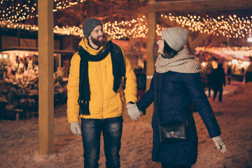 Obraz premium Photo of two adorable people guy lady walking lights midnight gifts market newyear evening enjoy snowy weather wear winter coats scarfs hats gloves outdoors