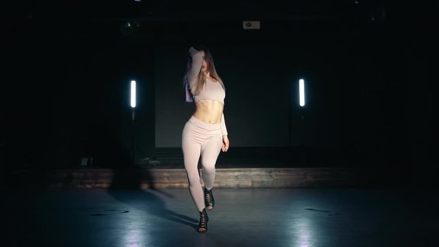 Girl dancing sexy dance on dark background. Woman in seductive outfit moves to the rhythm of music. Slow motion.