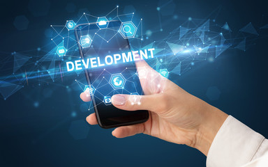 Female hand holding smartphone with DEVELOPMENT inscription, modern technology concept