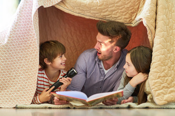 Vater und Kinder mit Taschenlampe beim vorlesen - obrazy, fototapety, plakaty