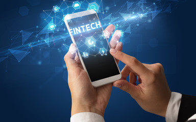 Female hand holding smartphone with FINTECH inscription, modern technology concept