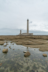 Fototapeta premium tall stone lighthouse with rocky shore tidal pools in foreground under a stormy sky