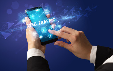 Female hand holding smartphone with WEB TRAFFIC inscription, modern technology concept