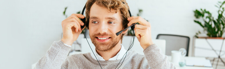 panoramic shot of happy bearded operator in brokers agency wearing headset