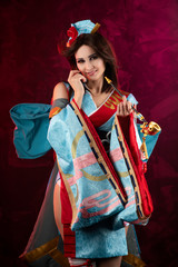 Beautiful leggy busty cosplayer girl wearing a stylized Japanese kimono costume cheerfully posing holding a fake pipe on a blue background.