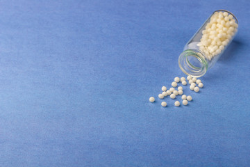 Homeopathic globules (pills) and glass bottle on blue background. The concept of healthcare and alternative herbal medicine: homeopathy and naturopathy. Flatlay, top view, copyspace for text.