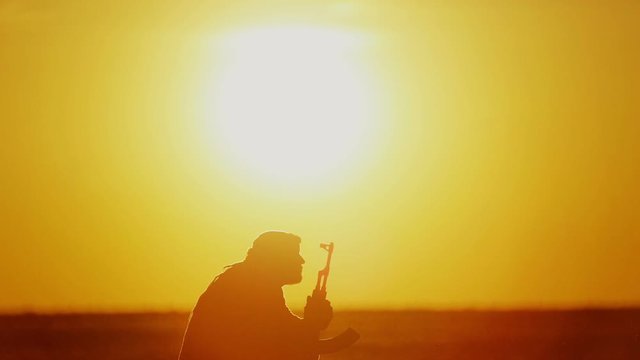 Islamic warrior with Kalashnikov at sunset day. Muslim fighter is training with a machine gun at sunset.