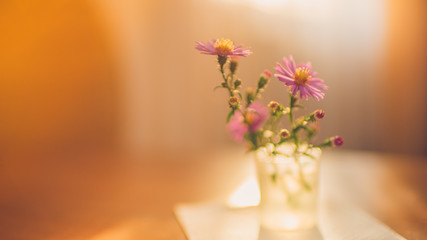 delicate purple flowers chrysanthemums in a little vase on a wooden sunny table.