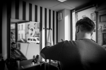 Closeup rear (back) view of man getting haircut in hair salon and reflection on the mirror