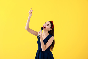 Beautiful young female singer with microphone on color background