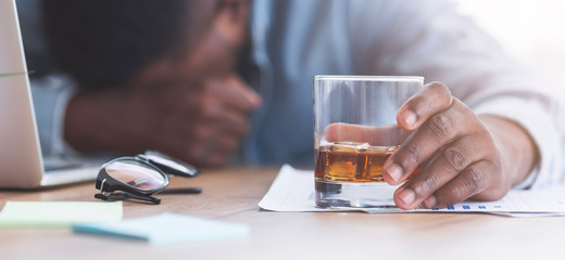 Drunk businessman sleeping at workplace with whiskey glass in hand