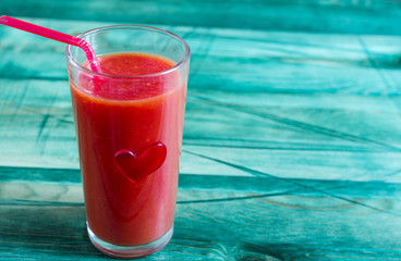 A glass of tomato juice and a red heart on a green background concept