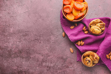 Bowls with different dried fruits and nuts on color background