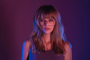 Fashion sexy young woman 20s girl model attractive face blond hairstyle wearing stylish trendy eyewear sunglasses looking at camera at purple violet neon light studio background, closeup portrait