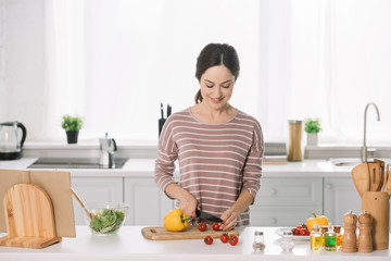 attractive young woman cutting fresh vegetables on chopping board