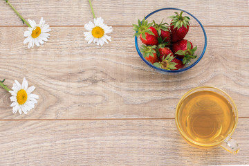 Glass cup of green tea, stawberries with white chamomile flowers on wooden background.