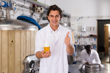 Man brewer in uniform with glass of beer holding thumb up