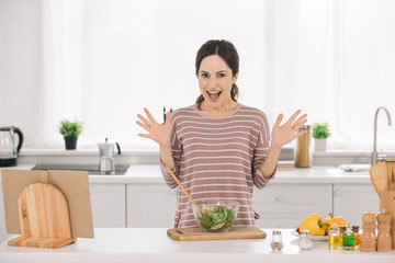 excited young woman showing wow gesture while standing near bowl with fresh vegetable salad