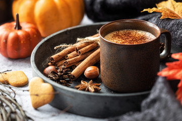 Thanksgiving concept - cup of hot frothy coffee in a rustic brown mug with cinnamon sticks,...
