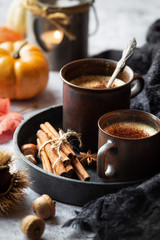 Fall time concept - two cups of cappuccino coffee with autumnal leaves, chestnuts, acorns and pumpkins at the background. Cold autumn days