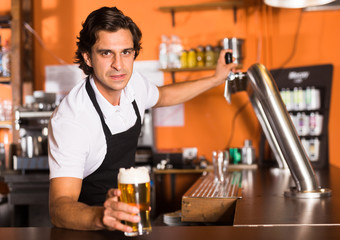 Positive man bartender offering glass of golden beer