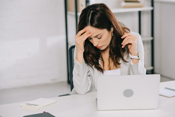 tired secretary suffering from headache while sitting at workplace and holding hand near head