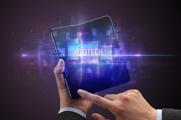 Businessman holding a foldable smartphone with BIOTECH inscription, new technology concept