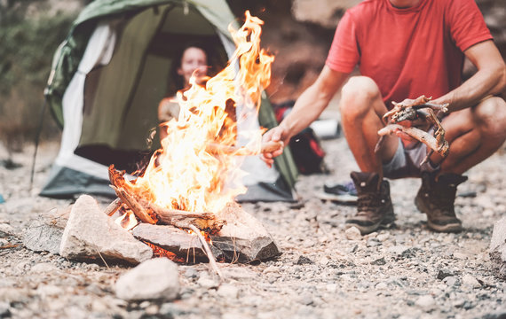 Happy couple making fire while camping in wild forest - Young people having fun traveling and campin