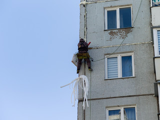 Fototapeta na wymiar Repair work at height. Worker insulates the seams of the facade of an old residential building. Maintenance of residential buildings