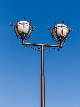 Street lamp against the blue sky. Two round frosted glass balls and dark ornate metal. Theme of improvement