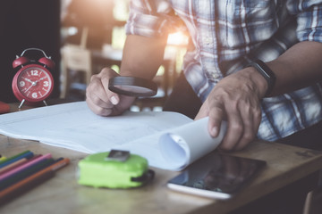 Engineers use a magnifying glass to review the house structure on the blueprint. Inspect and check the integrity before building the house for customers.