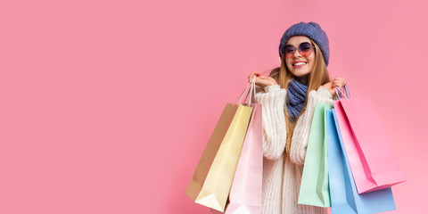 Positive girl in knitted hat and sunglasses holding shopping bags